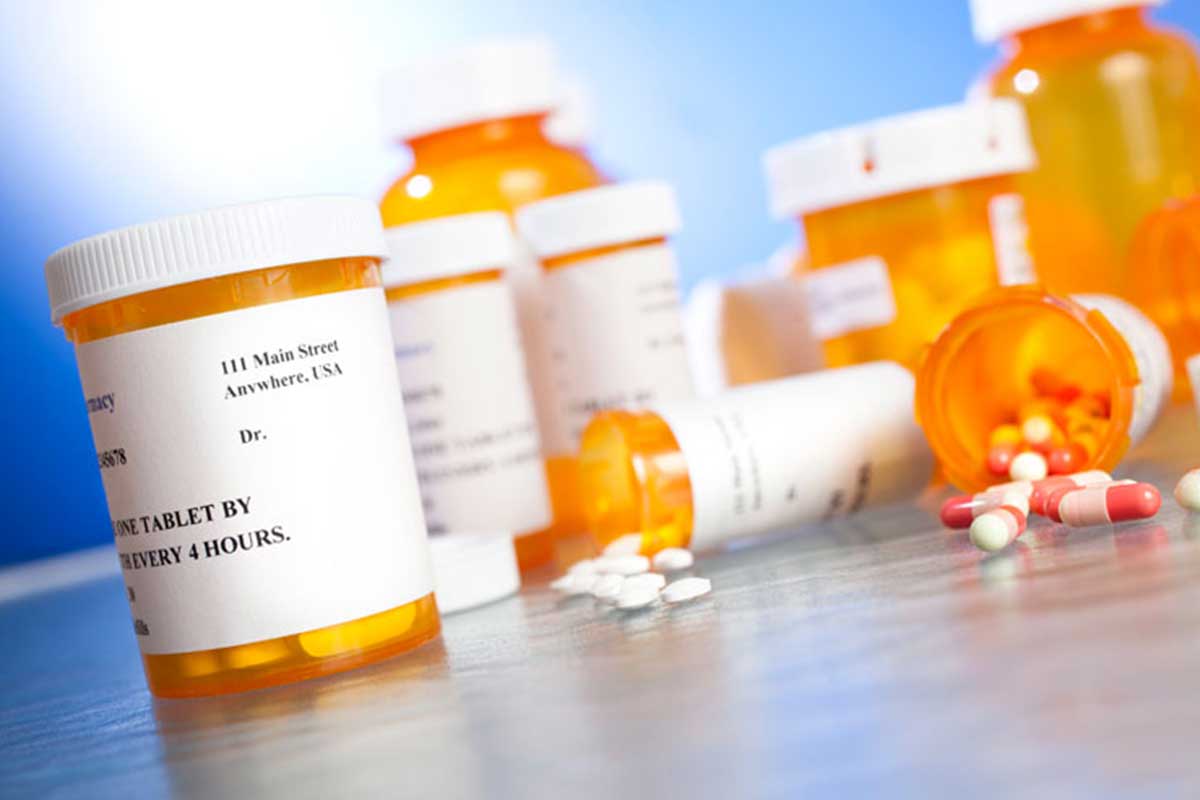 An angled photo of orange and white pill bottles and pills on a counter.