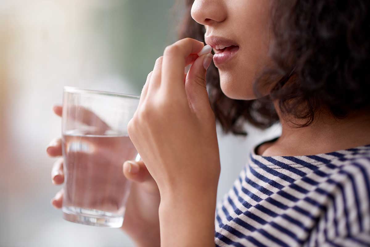 Close-up image of a teenage girl taking a medicine pill with a glass of water. Learn the dangers of teen medicine abuse.