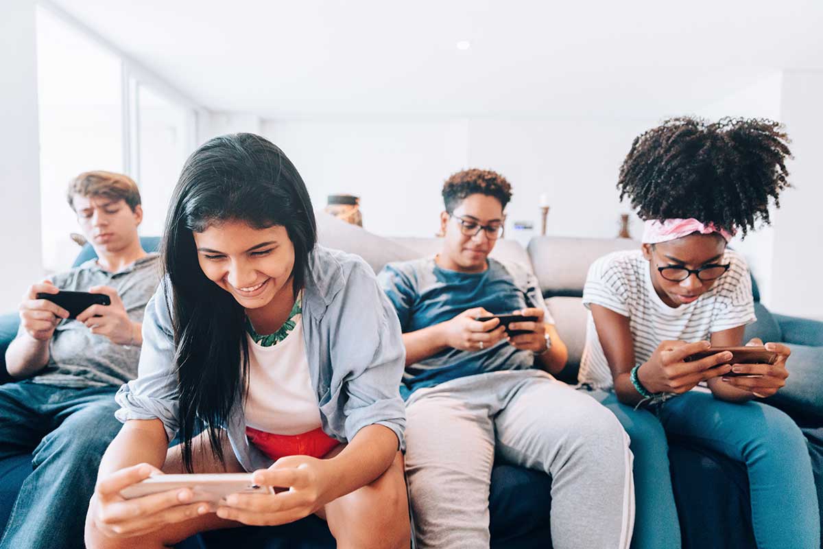 Group of teens on couch using their smartphones. Decode emoji drug codes and text slang to keep your teens safe.