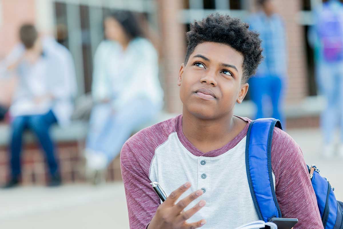 Teenage boy on school campus looks up in concentration.