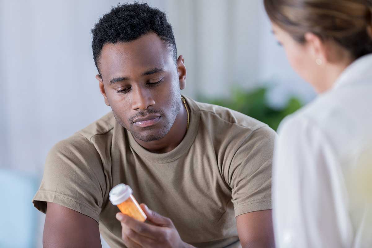 A young Black man examines a prescription bottle with his doctor. Find out how is the brain impacted by opioid misuse at RxGuardian.com