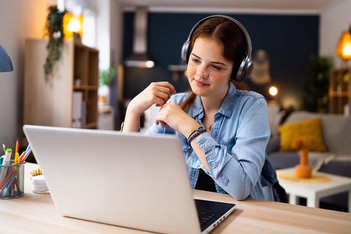 A young teenage girl sits in front of a laptop wearing headphones.
