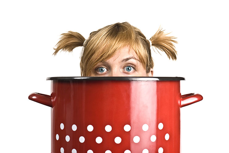 Image of the top of a teen girl's head looking over the edge of a cooking pot.