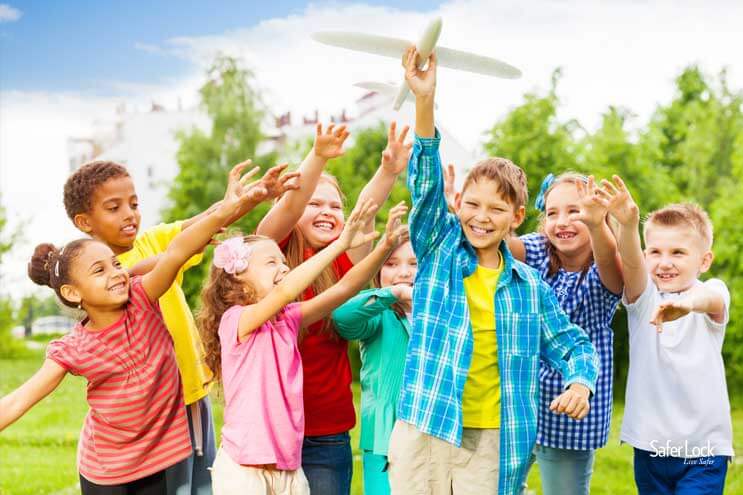 A group of happy kids plays with a toy airplane in a city park.
