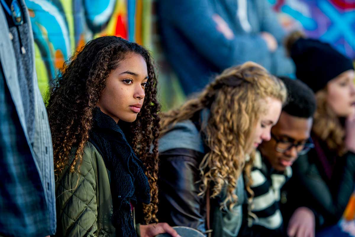 A multi-ethnic group of teenagers spendng time outside near a graffitt-sprayed building.