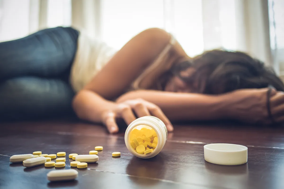 A woman laying on the floor with bottle of pills, concept of opioid overdose. Discover the findings of a 2023 opioid year in review.